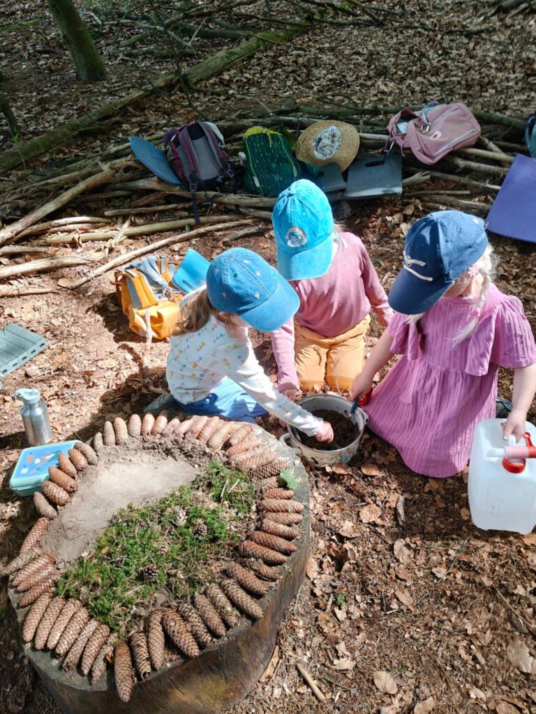 Kinder spielen mit Wasser und Erde an einem Kreis aus Zapfen