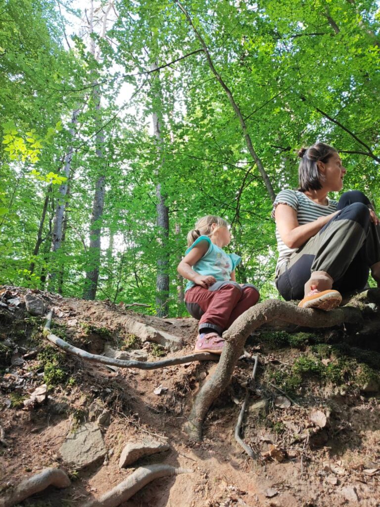 Erzieherin und Kind sitzen gemeinsam am Waldhang