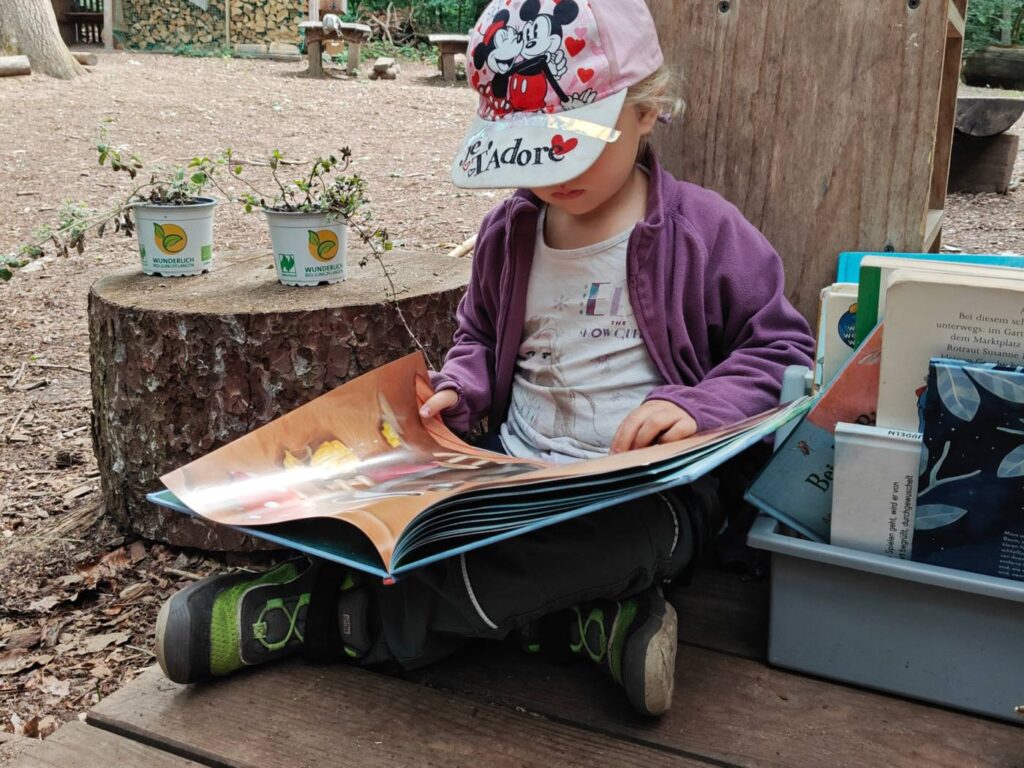 Ein Kind liest in einem Buch am Waldplatz